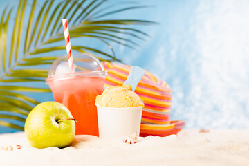 Enjoyment summertime - picnic on tropical beach with cold fruit cocktail, ice cream, sun hat under palm leaves with sand, sunny ocean view.