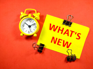 Education concept. Text WHAT'S NEW on colorful paper note with clock and paper clips on red background.