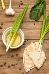 Green onions in bowl with olive oil. Pieces of pita, allspice and garlic on table