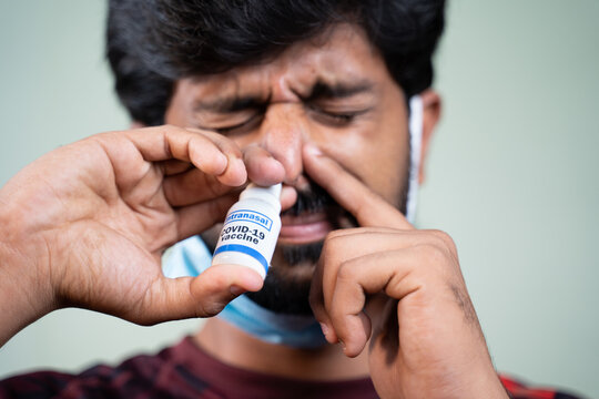 Close Up Head Shot Of Young Man By Removing Medical Face Mask Inhaling Coronavirus Covid-19 Nasal Spray - Concept Of Covid Intranasal Vaccine.