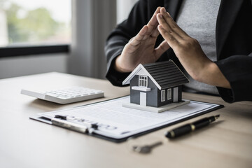 A small gray model house is an example of a home in a housing project, an insurance salesperson is doing a symbolic home protection act in home insurance. Real estate leasing concept.