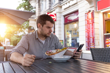 Mann isst einen Döner und schaut dabei auf sein Smartphone