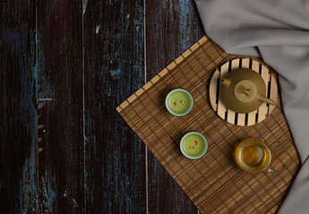Chinese Tea Ceremony. Brown ceramic teapot and turquoise teacup. Green tea on bamboo mat on aged wooden table. Top view. Copy space