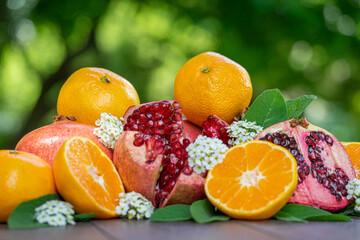 Cut Open Pomegranates and Oranges on a Wooden Table Outside with White Flowers