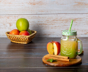 Basket of green and red apples with glass with cold apple juice on wooden background