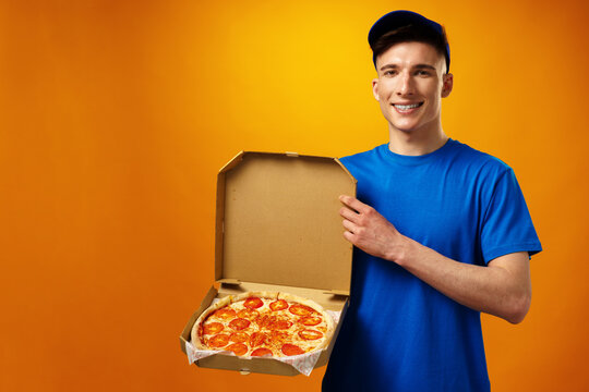 Happy Young Delivery Man Holding Pizza Box Against Yellow Background