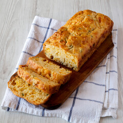 Homemade Cheesy Bread Loaf on a rustic wooden board on a white wooden background, side view.