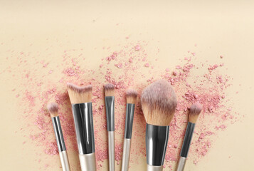 Makeup brushes and scattered eye shadow on beige background, flat lay. Space for text