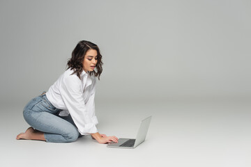 Pretty woman in white shirt and jeans using laptop on grey background