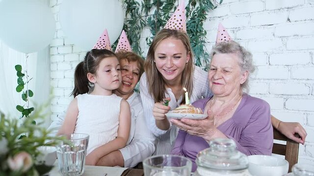 Celebration and family concept. Young girl lights a candle on birthday cake celebrating old grandma 85th birthday all together four woman generation. Female family enjoy, respect and warm relation
