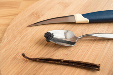 Vanilla seeds on a spoon, next to a stick and a knife. Blurred background