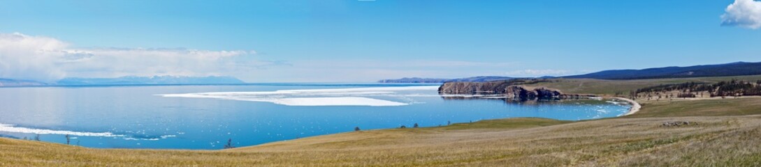 Baikal Lake in May. Panoramic view on the Small Sea Strait with melting ice off the coast and meadows of Olkhon Island with grazing herds. Beautiful landscape. Natural spring background
