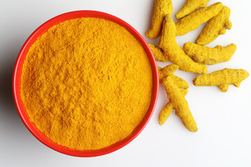 Turmeric powder in a  bowl next to turmeric roots 