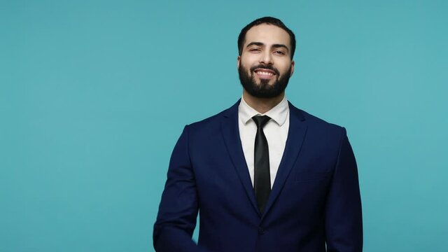 This is me! Proud handsome brunette bearded man in black suit smiling happily and pointing himself, feeling confident, egoistic person. Indoor studio shot isolated on blue background.