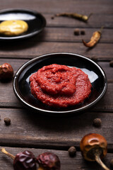 Closeup of dark plate full of ketchup, dry pepper,peppercorns and plate of mustard on the backgrund