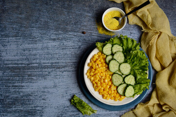 Top view of a plate with corn, cucumbers, lettuce and spices on a blue background. Layout, copy space