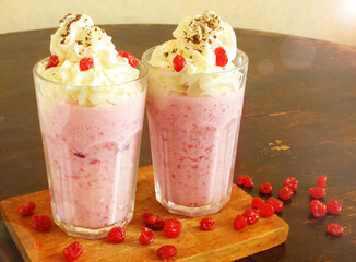 Strawberry milkshake made from fresh strawberries with whipped cream, prepared at home. Cocktail in two glass glasses, decorated with chocolate chips, dried cherries