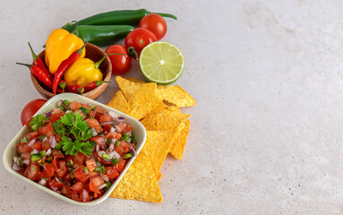 Mexican appetizer Pico de Gallo in a bowl and ingredients on the table.