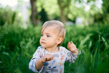 Serious kid sits in the tall grass. Portrait