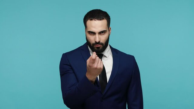 Hey you, come to me! Handsome brunette man with beard in formal black suit looking with serious expression at camera, doing inviting gesture. Indoor studio shot isolated on blue background.