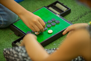 Closeup of kids hands playing reversi or othello traditional strategic board game by thinking, planing and use fingers flip the black reversible disc. Cognitive skills, Mind sport, Competitive concept