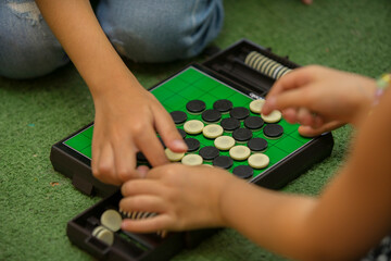 Closeup of kids hands playing reversi or othello traditional strategic board game by thinking, planing and use fingers flip the black reversible disc. Cognitive skills, Mind sport, Competitive concept - obrazy, fototapety, plakaty