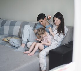 family photo, dad does his daughter's hair, kisses her, sits on the couch with his wife and daughter