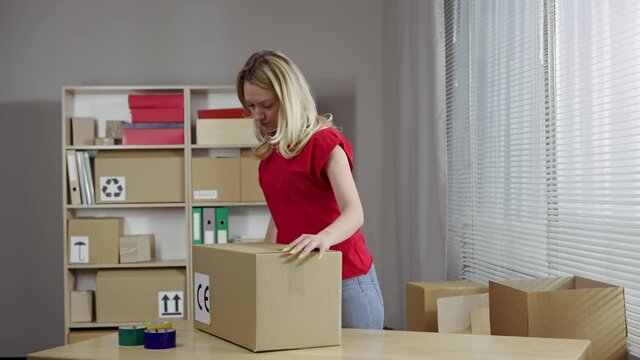 Young female online store owner, warehouse worker, merchant seller seals with tape package, preparing delivery parcel box. Post service. Close up. Slow motion ready 59.94fps.