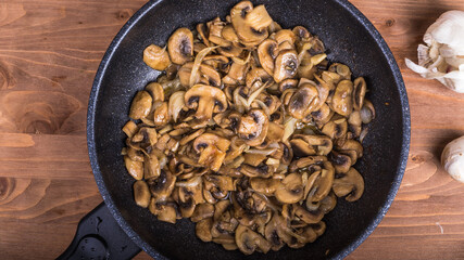 Fried mushrooms in a pan on the table, close-up. Champignon mushrooms, cut into slices, are fried in a pan. Vegetarian dish, top view