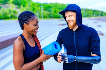 smiling young mixed race couple in sportswear warming up outdoors sity background early morning