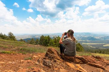 Naklejka premium Tourist girl photographing with vintage photo camera at the top of the mountain peak