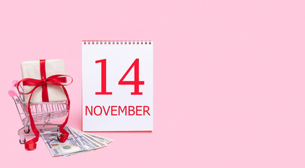 A gift box in a shopping trolley, dollars and a calendar with the date of 14 november on a pink background.