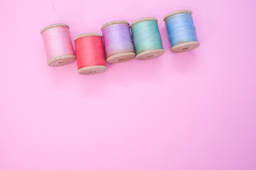 Colorful sewing threads isolated on a pink background with free space for text