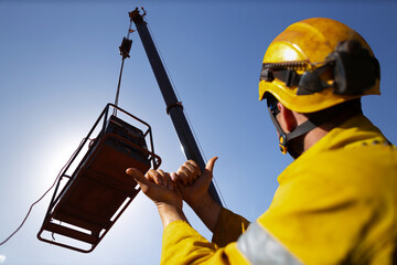 Safe work practice rigger wearing fall protection helmets giving crane operator hand signal by...