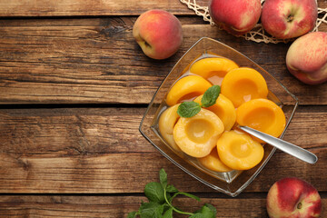 Canned peach halves in glass bowl on wooden table, flat lay. Space for text