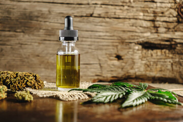 a vial with a dropper of cannabis concentrate cbd stands next to dried marijuana buds and a...