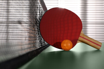 Racket and ball near net on ping pong table indoors