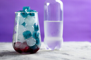 Blue and white ice in a glass, behind there is a bottle of lemonade
