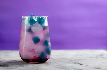 pink cocktail with blueberries stands on the table. There is blue and blue ice in the glass.