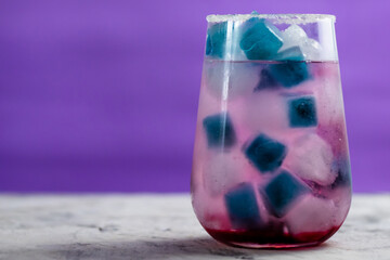 pink cocktail with blueberries stands on the table. There is blue and blue ice in the glass.