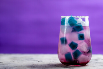 pink cocktail with blueberries stands on the table. There is blue and blue ice in the glass.