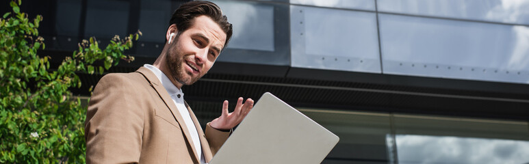 low angle view of businessman in earphones having video call on laptop outside, banner.