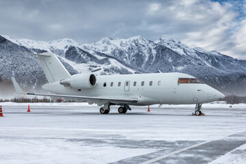White luxury corporate business jet on the winter airport apron on the background of high scenic...