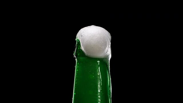 Beer foam escapes from bootle on black background