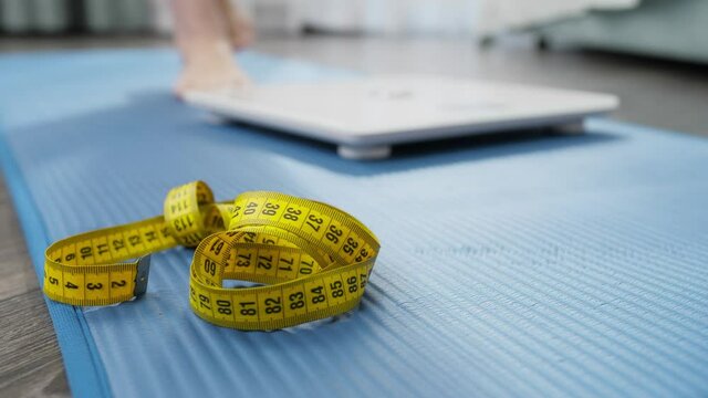 Closeup of barefoot woman weighting on scales on fitness mat after doing exercise or fitness. Concept of dieting, loosing weight and healthy lifestyle.