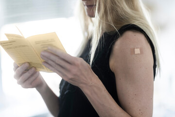 Junge Frau mit Pflaster auf dem Arm hält Impfausweis in der Hand,  nach Impfung gegen Covid19
