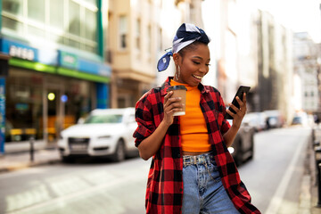 Fototapeta na wymiar Young african woman using the phone while drinking cofee. Beautiful woman drinking coffee outdoors.
