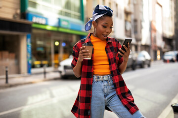 Young african woman using the phone while drinking cofee. Beautiful woman drinking coffee outdoors.