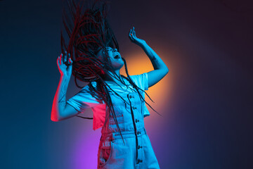 Caucasian young woman's portrait on dark studio background in neon. Concept of human emotions, facial expression.