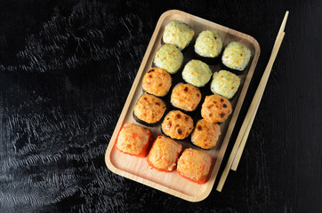A set of various rolls with chopsticks in a wooden bamboo plate on a black wooden background.